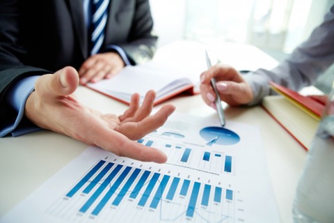 Image of two people's arms and hands on a table going over graphs and statistics.